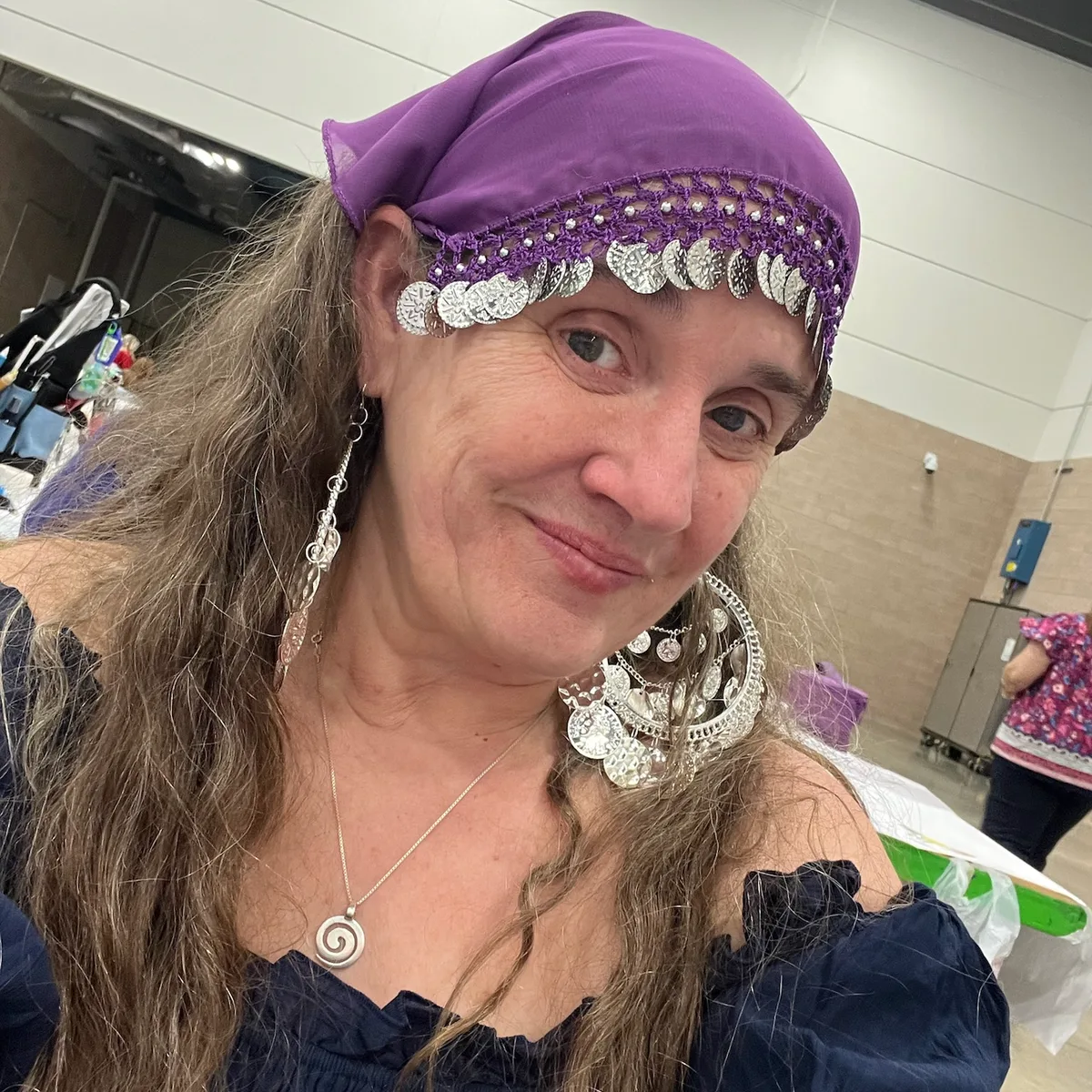 Jolynn wearing a purple headscarf with coin trim and large hoop earrings.
